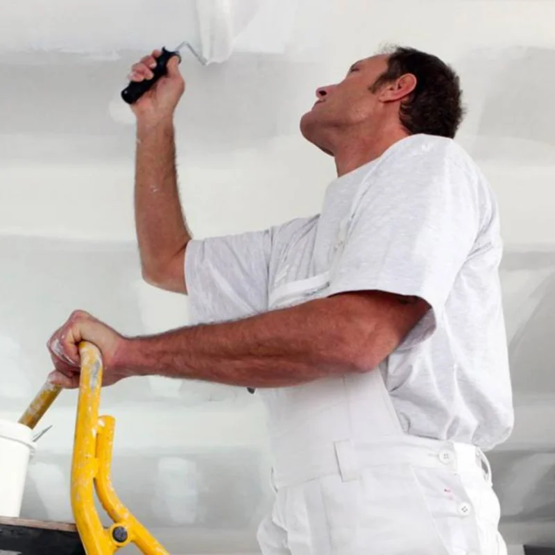 Schilder in witte kleding werkt met een roller aan een wit plafond